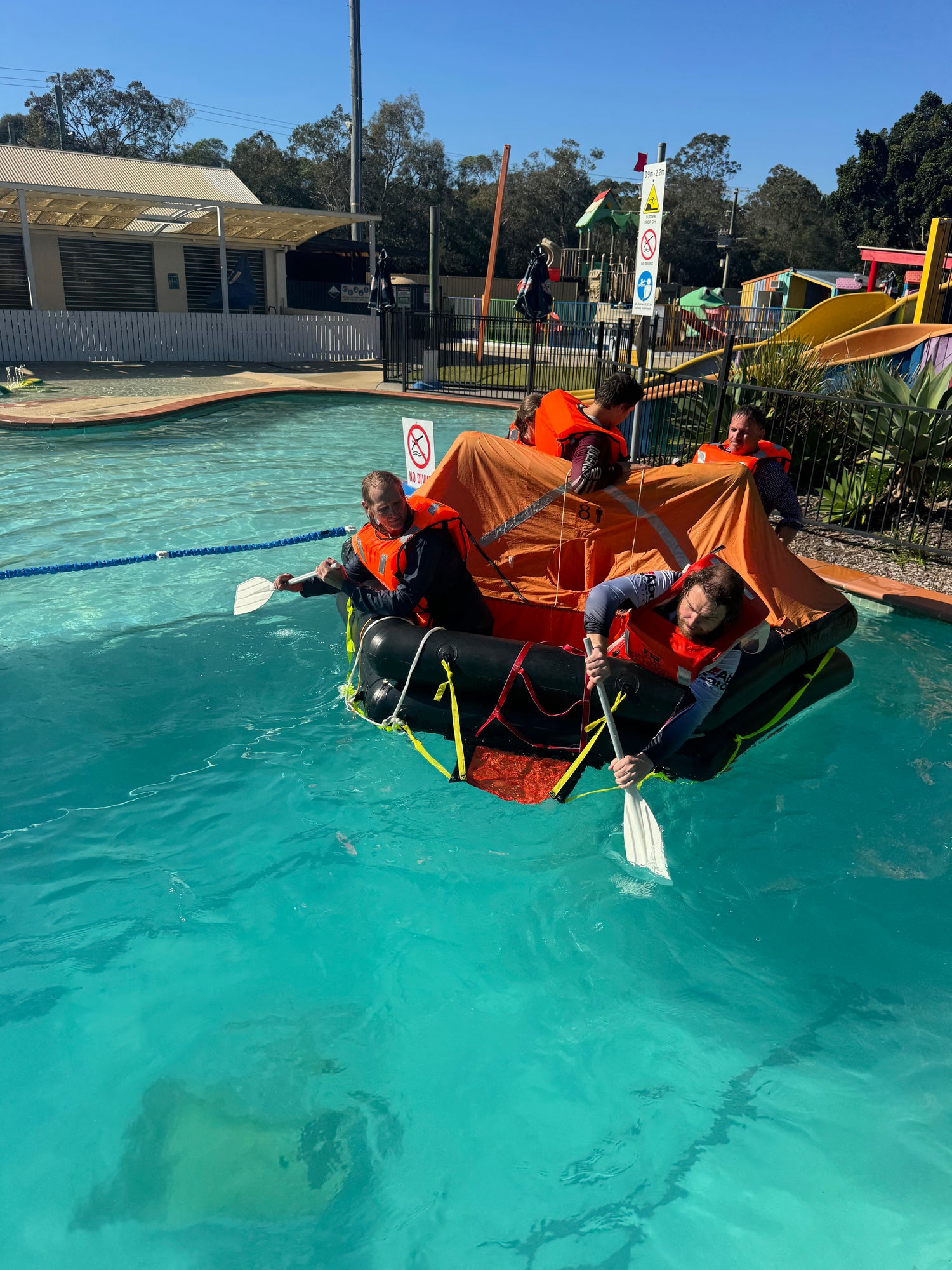 Students in lifejackets boarding and paddling a life raft during survival training